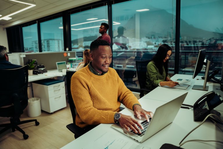Mixed race male typing email to colleagues and clients regarding new idea for project sitting concentrating in office